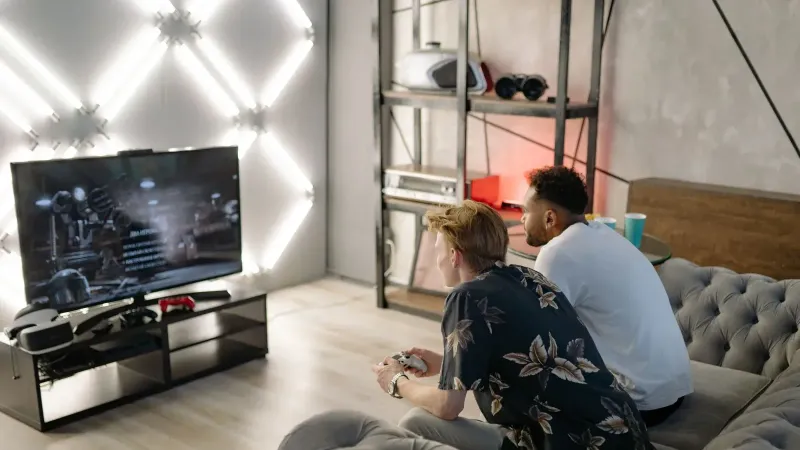 Dos hombres jóvenes que juegan juntos en una elegante sala de estar moderna con un televisor grande.