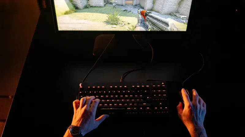A gamer intensely playing a first-person shooter game on a computer setup indoors at night.