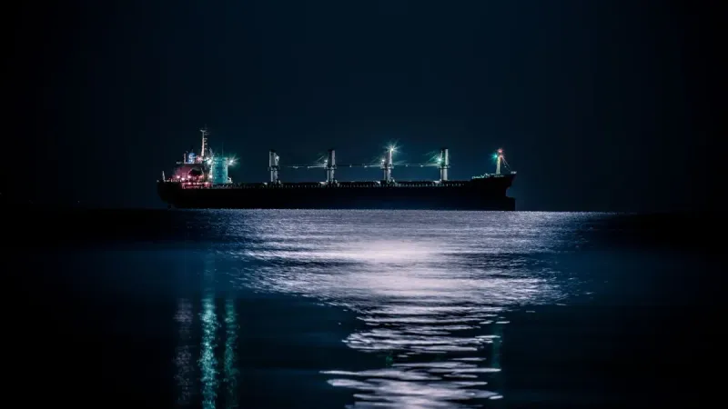 Una tranquila escena nocturna de un buque de carga flotando en un océano tranquilo bajo un cielo estrellado.