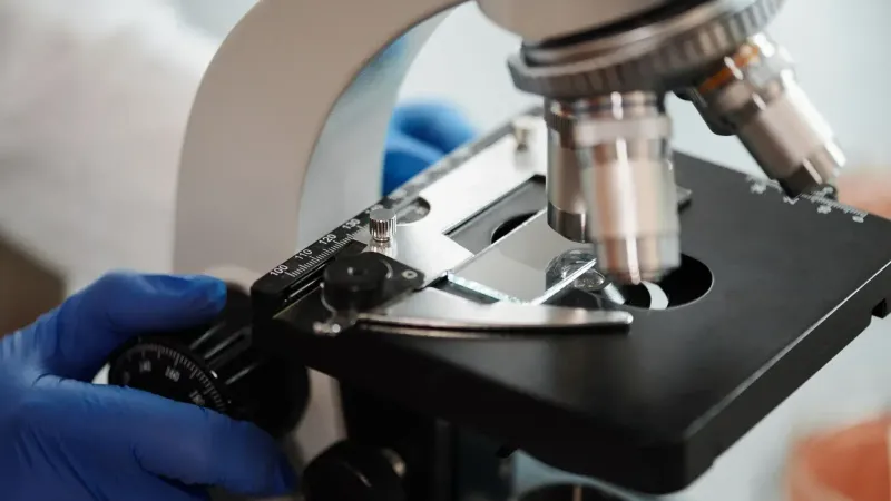 Imagen de primer plano de la mano enguantada de un científico ajustando un microscopio en un laboratorio de investigación.