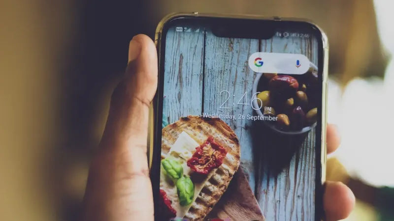 Close-up of a hand holding a smartphone displaying a food image on its screen, indoors.
