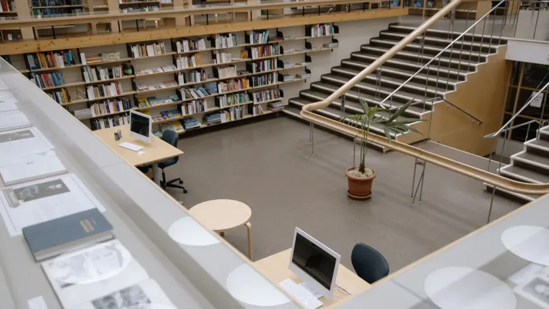 Amplio interior de la biblioteca universitaria con estanterías, escritorios y una escalera para estudio e investigación.