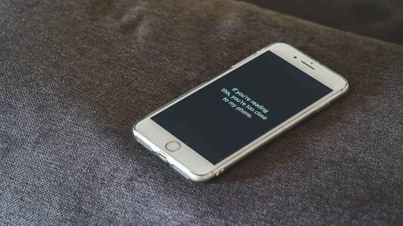 A smartphone with a humorous lock screen message placed on a grey couch, emphasizing privacy.
