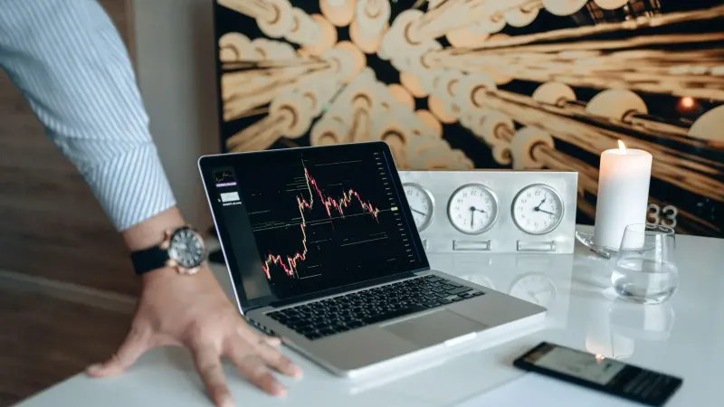 Un escritorio contemporáneo con dispositivos tecnológicos y una computadora portátil que muestra un gráfico de acciones.