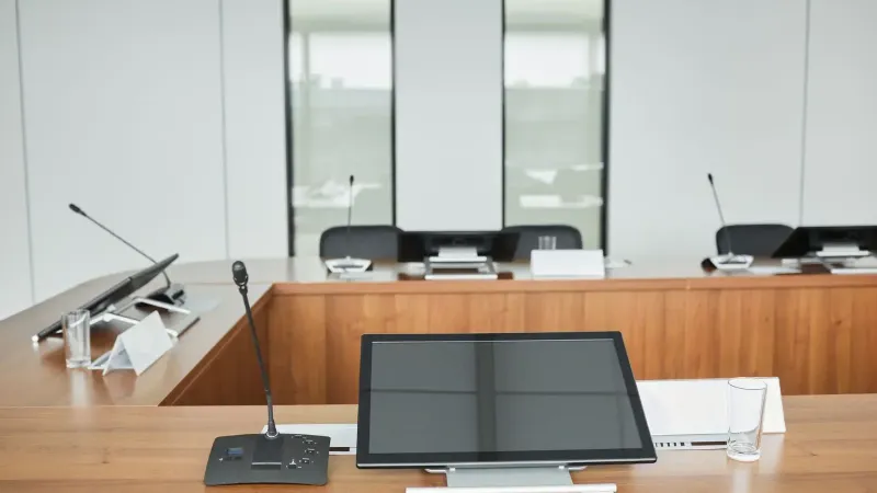Empty conference room setup with microphones, monitors, and sleek wooden tables ready for meetings.