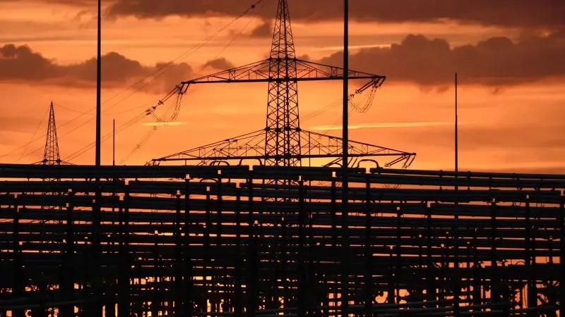 Silhouetted electric tower against vivid sunset sky, highlighting urban infrastructure.