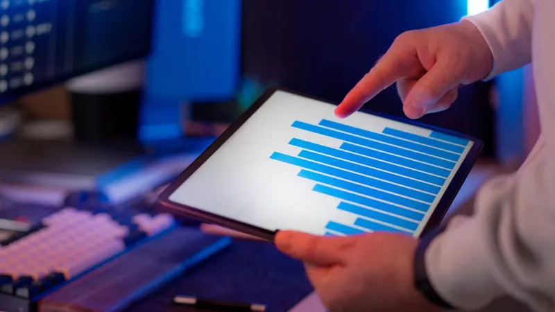 Business professional analyzing bar chart on tablet in office setting, highlighting data insights.