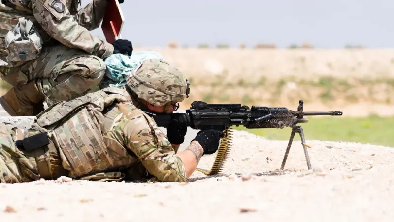 US soldier in camouflage uniform using a machine gun in outdoor military training.