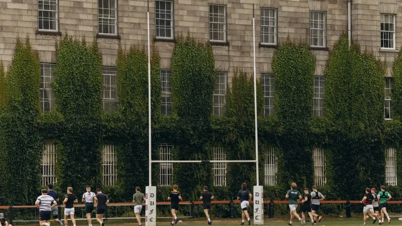 Rugby players practice on lush grounds of Trinity College Dublin.