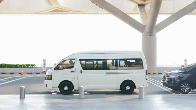 A white minivan parked at a modern airport terminal drop-off zone, ideal for travel and transport concepts.
