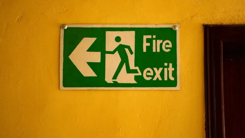 Fire exit sign on a yellow wall, indicating safety and emergency exit direction.