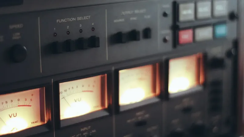 Primer plano de una grabadora de cinta vintage con medidores VU iluminados y controles de función.