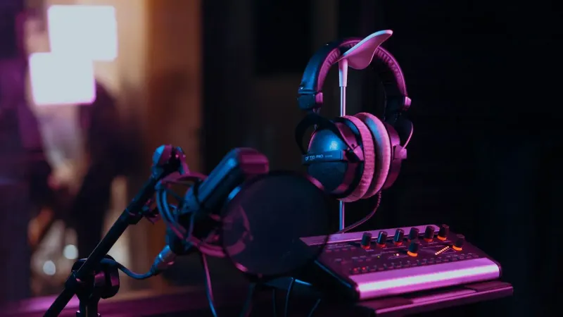High-quality audio recording studio setup with a microphone, headphones, and mixer board in dim lighting.