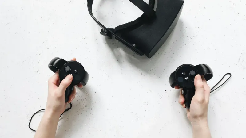 Two hands hold virtual reality controllers above a VR headset, showcasing modern technology.