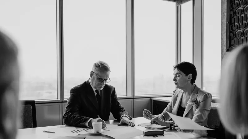 Black and white image of a business meeting with diverse professionals collaborating.