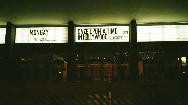 Outdoor view of an illuminated theater marquee displaying movie titles at night.