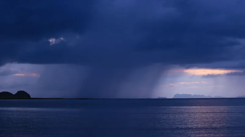 A breathtaking view of rain clouds looming above the calm ocean during twilight, creating a serene seascape.