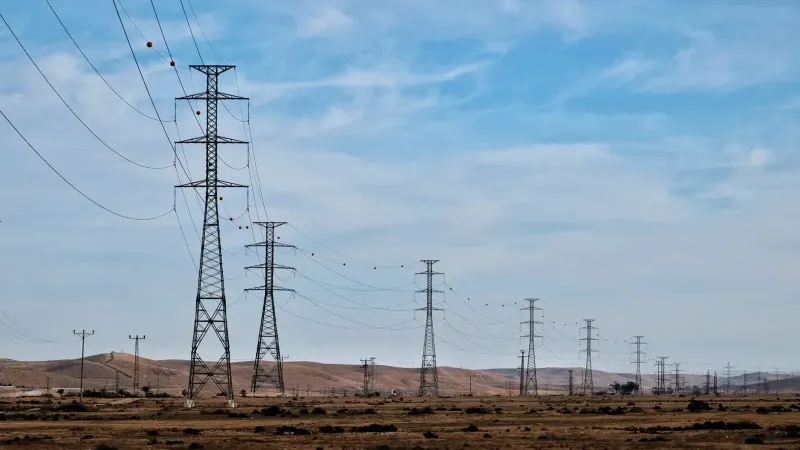 Transmission towers in a desert landscape with blue skies, showcasing energy infrastructure.