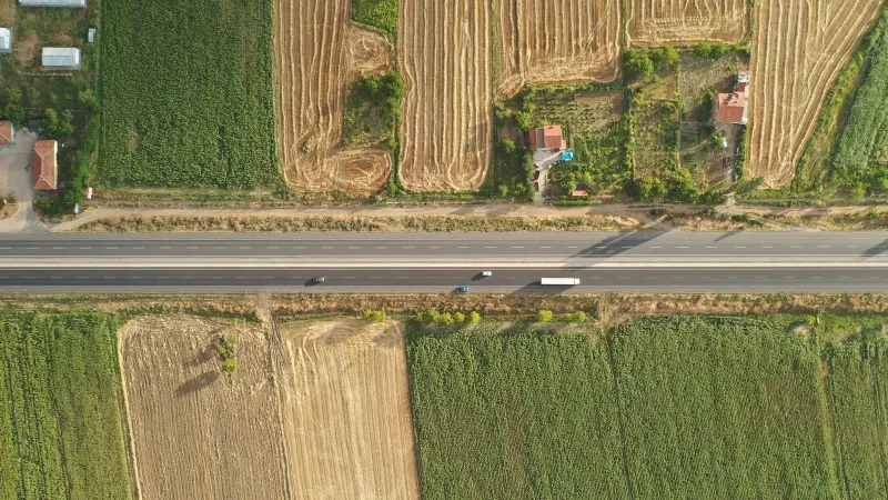 Aerial shot of a rural road cutting through lush fields, showcasing the beauty of the countryside from above.