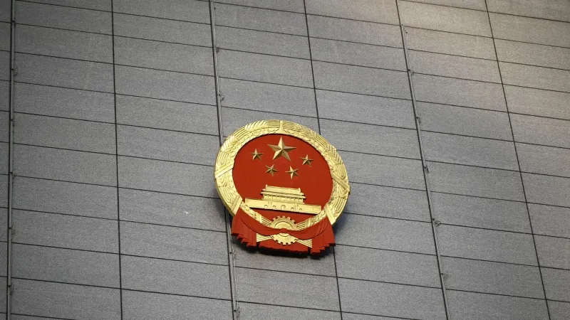 Close-up del emblema nacional chino en una gran fachada de edificio de hormigón, que simboliza la presencia del gobierno.