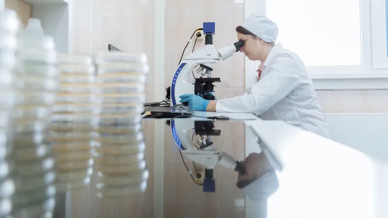 Female scientist using a microscope in a laboratory environment, focusing on research.