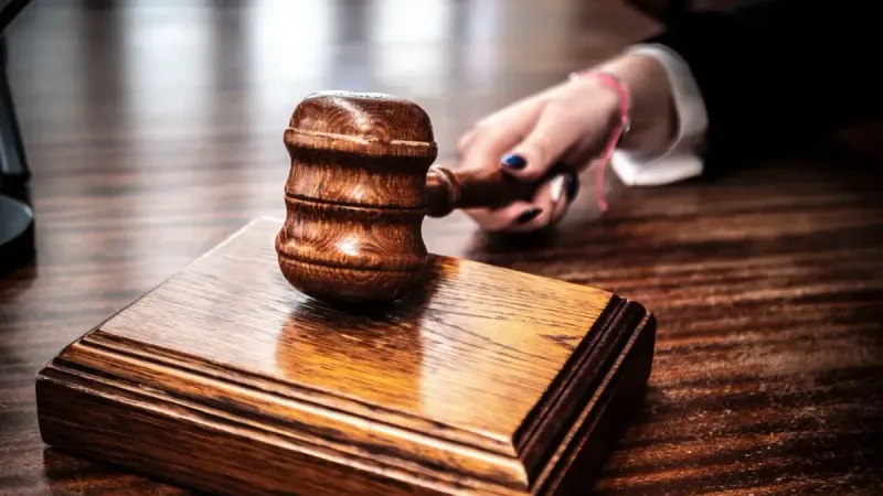 Imagen de primer plano de un mazo de madera sostenido a mano sobre un escritorio en un tribunal.