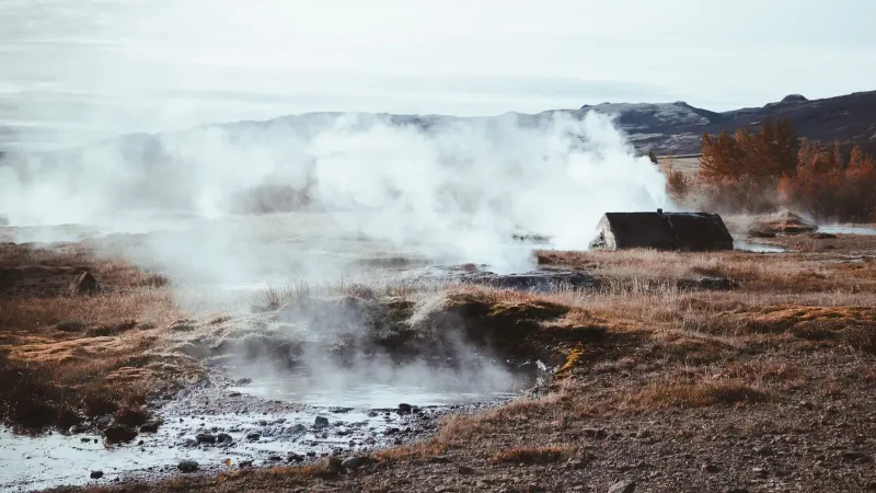 A serene geothermal field with steam rising amid autumnal surroundings. Perfect for nature and travel themes.