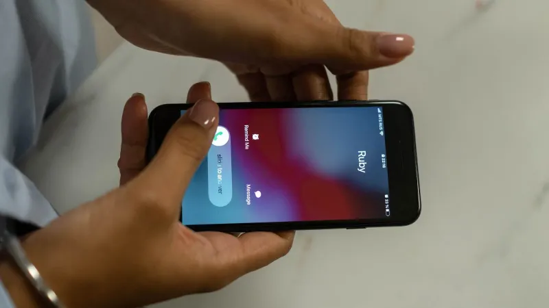 Close-up image of hands holding a smartphone receiving a call from Ruby on a marble surface.