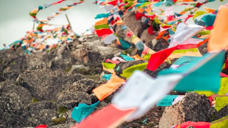 Vibrant Tibetan prayer flags fluttering on a rocky hillside in Garzê, China.
