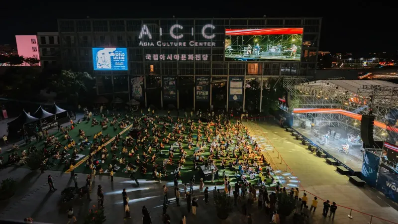 A vibrant outdoor concert at the Asia Culture Center, bustling with a lively crowd at night.