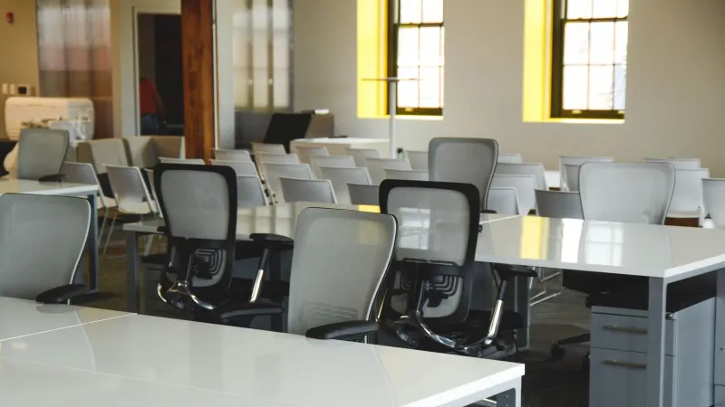 Spacious open office workspace with desks, chairs, and natural lighting.