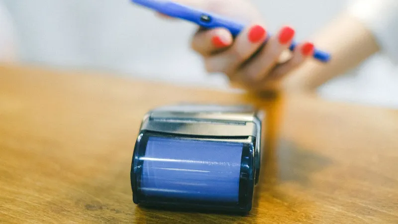 Close-up of hand using smartphone for contactless payment at a terminal on wooden surface.