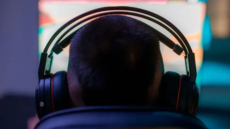 A man wearing headphones intently playing a video game on a computer in a dark room.