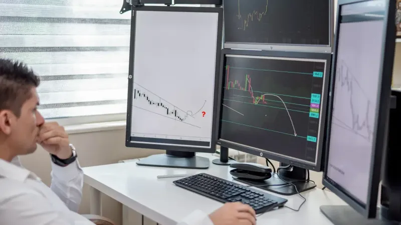 Business professional analyzing financial data on multiple computer monitors at his workspace.