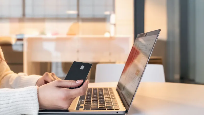 A woman using a credit card and laptop for online shopping in a modern indoor setting.