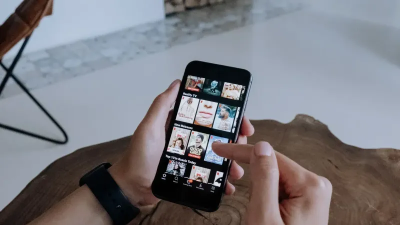A person using a smartphone to explore and select shows on a streaming platform indoors.