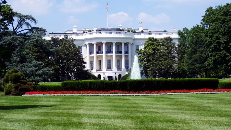 Iconic view of the White House with lush gardens and a central fountain on a sunny day.