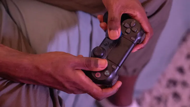 Manos agarrando un controlador de juego, involucrado en un videojuego en interiores.