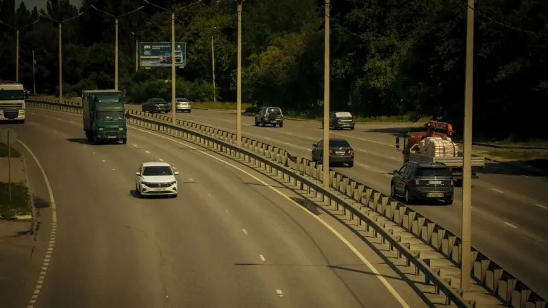 Múltiples vehículos que viajan en una amplia carretera rodeada de árboles en un día soleado.