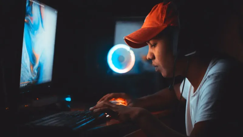 Un joven con una gorra naranja se centró en jugar por la noche con iluminación de computadora.
