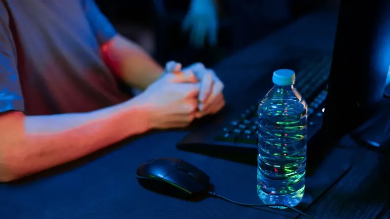 Una vista de cerca de una configuración de juego con una botella de agua y un mouse de computadora en un entorno con poca luz.
