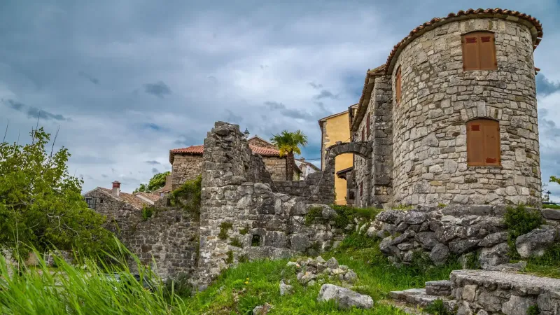 Historic stone buildings amidst vibrant greenery under a cloudy sky.