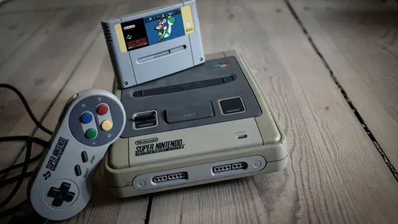 From above of aged video game console with cassette and controller with colorful buttons on wooden surface