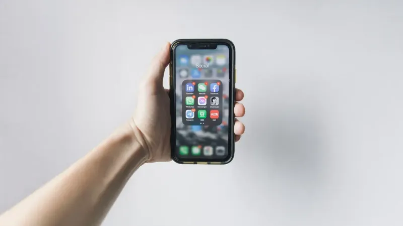 Mano que sostiene el teléfono inteligente que muestra las aplicaciones de redes sociales en la pantalla de inicio.