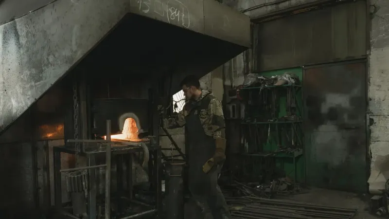 Herrero trabajando en una fragua brillante, moldeando metal calentado en un entorno industrial.