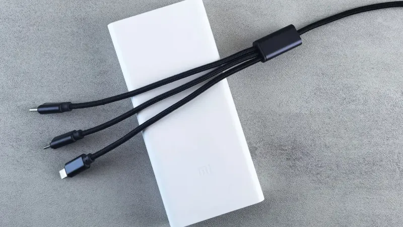 Un elegante banco de energía blanco con un cable multiconector negro colocado sobre una superficie gris texturizada, enfatizando la tecnología moderna.