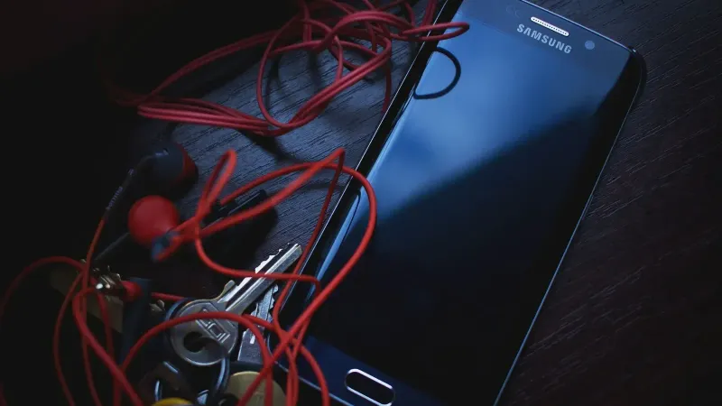 Smartphone Samsung con auriculares rojos y llaves sobre una mesa de madera, en iluminación natural.