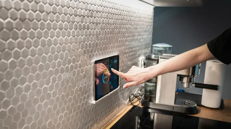 A modern kitchen with a touchscreen smart home control panel integrated into a hexagon-patterned wall.