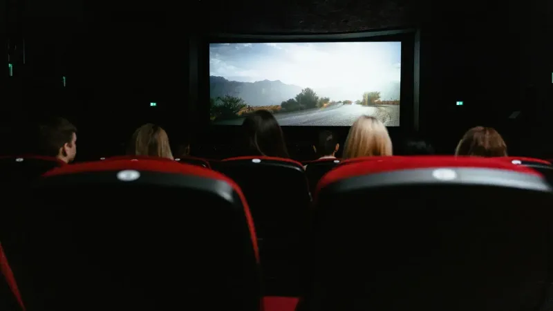 Vista desde atrás de gente viendo una película en un cine con asientos rojos y una pantalla grande.