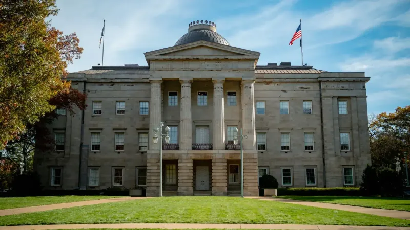 Front view of the historic North Carolina State Capitol in Raleigh, showcasing neoclassical architecture under a blue sky.